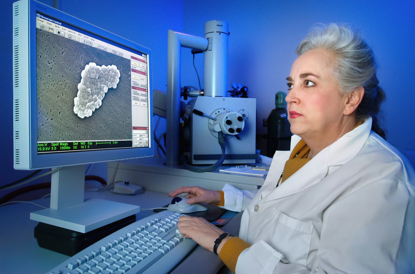 Scientist in lab coat working at computer with microscope.